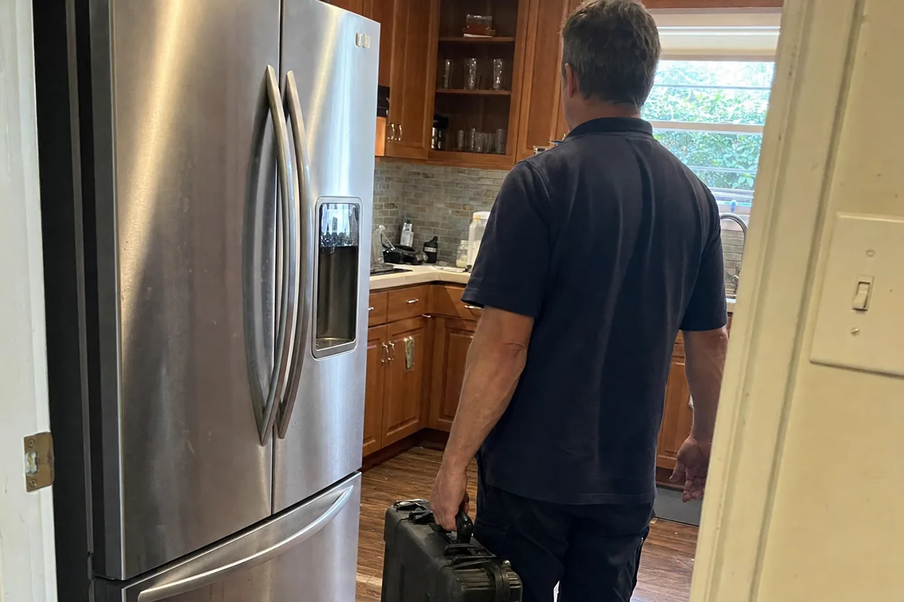 Mirrored view of a service call arriving through a kitchen doorway, tool case in hand