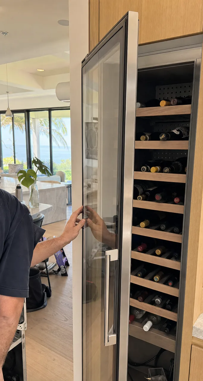 Mirrored narrow crop of a glass wine cabinet door open against a bright kitchen beyond