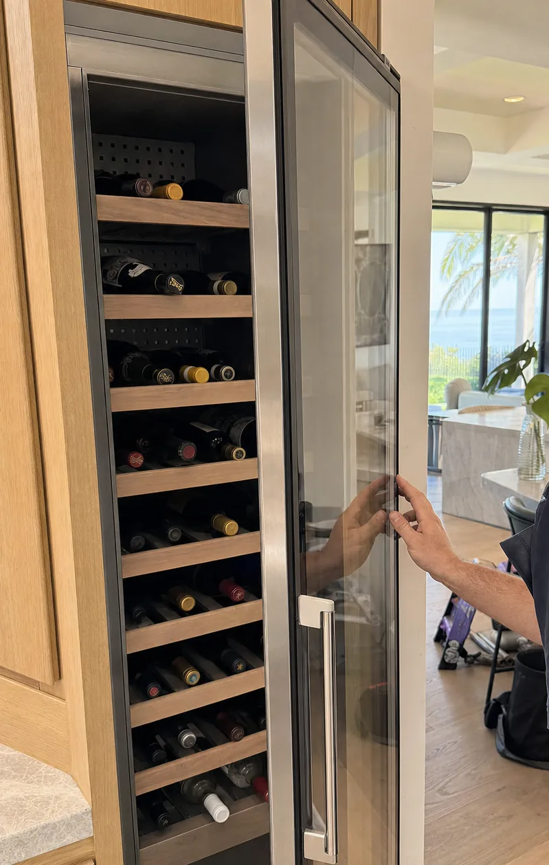 Close frame of racked bottles behind the open glass door of a wine cabinet